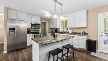 Cocina moderna con armarios blancos, electrodomésticos de acero inoxidable y una isla de mármol con taburetes de bar.