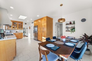 A modern kitchen with wooden cabinets, a central island, and a dining area with a table set for four. - SAN DIEGO SPA VILLA - Cozy Yard, Firepit, Rec Room (San Diego)