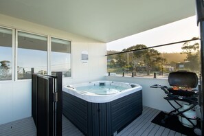 A hot tub on a balcony with a grill and a view of trees and buildings.