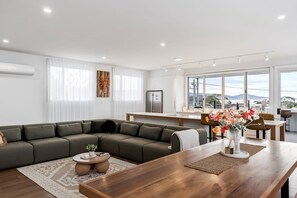A modern living room with a sectional sofa, a wooden dining table, and a kitchen area in the background.