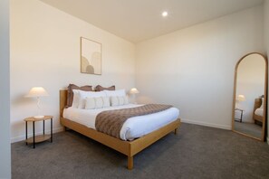A bedroom with a wooden bed, two bedside tables with lamps, a large mirror, and a framed picture on the wall. - The Bunkhouse - Bicheno Accommodation (Bicheno)