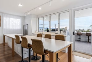 A modern kitchen with a central island, bar stools, and a view through large windows.