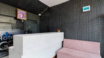 A hotel reception area with a marble counter, a pink sofa, and a textured wall.