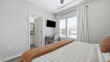 A bedroom with a bed, a desk, a chair, a television, and a window with curtains.