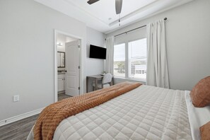 Un dormitorio con cama, escritorio, silla, televisión y ventana con cortinas.