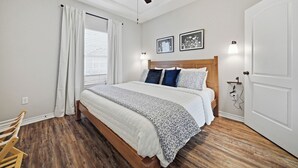 Un dormitorio con cama, ventilador de techo, ventana con cortinas y una puerta.