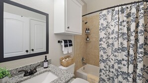 Un baño con lavamanos de encimera de granito, inodoro blanco, ducha con cortina estampada y espejo con marco negro.