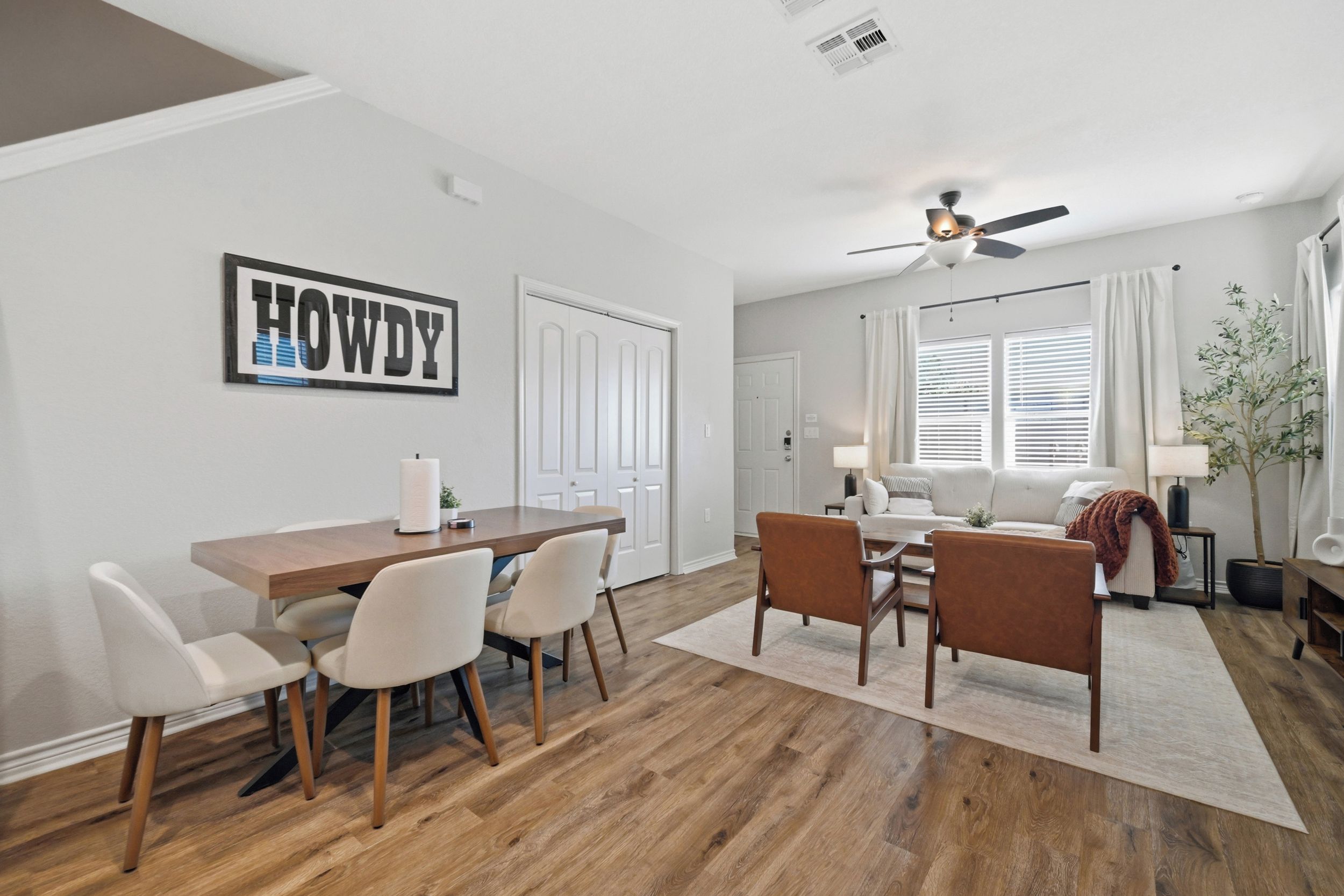 A modern living room with a sofa, a dining table with chairs, and a ceiling fan.