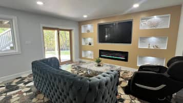 Una sala de estar con un televisor de pantalla plana grande, un sofá, una mesa de centro y un piso con diseño.