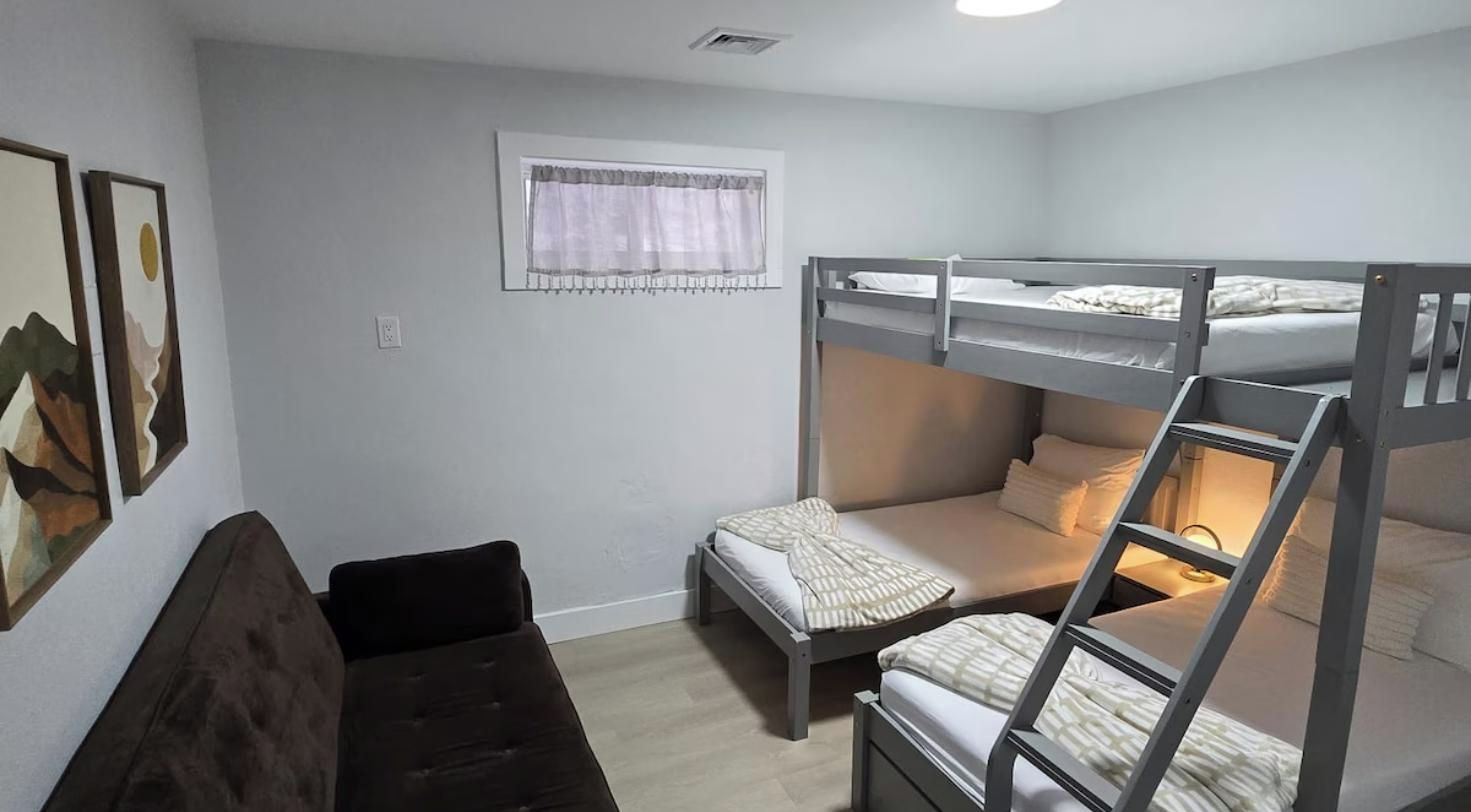 Una habitación con literas, una cama individual, un ventanal con cortina y un respiradero en la pared.