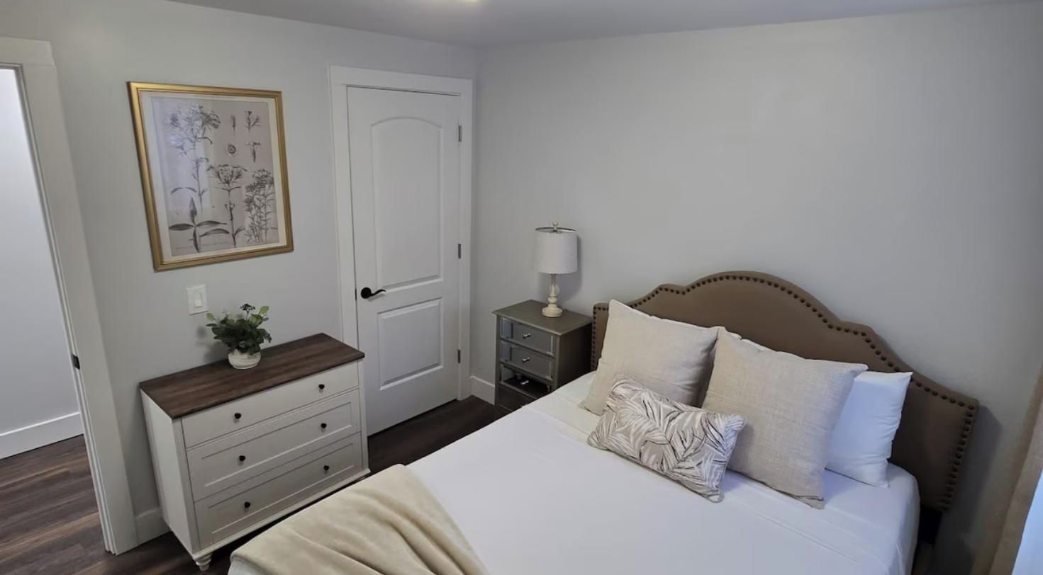 Ein Schlafzimmer mit Bett, Nachttisch, Lampe und einem gerahmten Pflanzenprint an der Wand.
