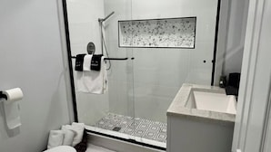 A modern bathroom with a glass shower enclosure, a white sink, and a patterned shower floor. - Catskills Stone Getaway - 6BR, Sleeps 14, Game Room, Firepit, Near Skiing (Purling)