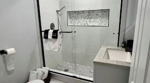 A modern bathroom with a glass shower enclosure, a white sink, and a patterned shower floor. - Catskills Stone Getaway - 6BR, Sleeps 14, Game Room, Firepit, Near Skiing (Purling)