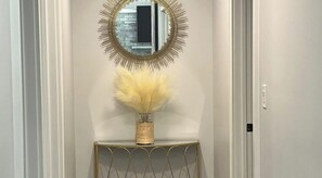 A hallway with a mirror on a console table, a vase with dried pampas grass, and a door with a light switch.