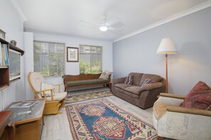 A living room with a sofa, armchair, a patterned rug, a floor lamp, and a ceiling fan. - 1BR Tighes Hill Retreat with Private Courtyard (Tighes Hill)