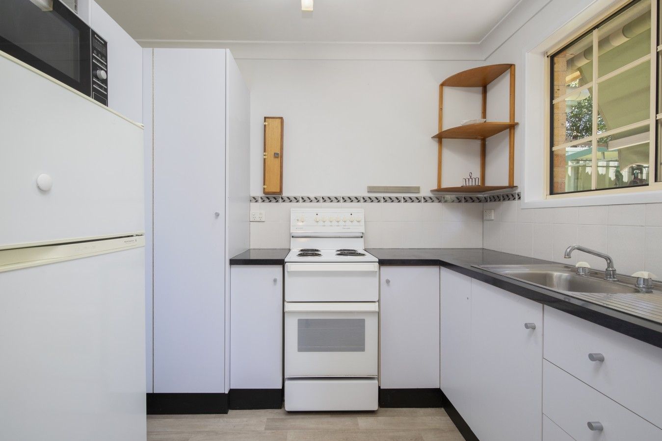 A kitchen with white cabinets, a stove, a sink, and a window with a view.