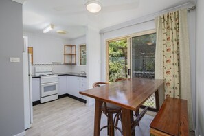 Une cuisine compacte avec un coin repas, des meubles blancs, une table en bois et une vue à travers une porte vitrée.