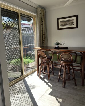 A room with a sliding glass door leading to a patio, a table with two chairs, and a framed picture on the wall. - 1BR Tighes Hill Retreat with Private Courtyard (Tighes Hill)