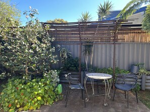 Un espace patio avec une table et deux chaises, entouré de plantes et d’une clôture en bois.