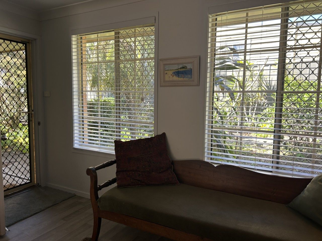 A room with a wooden bench, two windows with blinds, a door, and a framed picture on the wall.