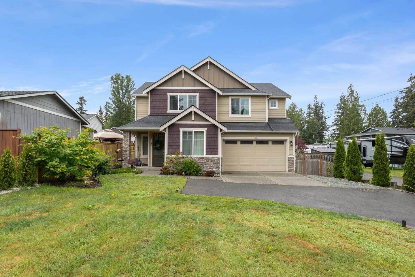 Una casa de dos pisos con garaje, un porche delantero y un césped bien cuidado.