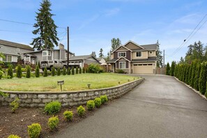A residential street with houses, a driveway, and a stone retaining wall. - Fully Furnished 5BR 3 Baths Family Home in Everett (Snohomish County)