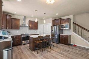 A modern kitchen with a central island, stainless steel appliances, and a staircase leading to a second floor.