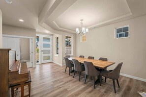 A dining area with a wooden table and chairs, a piano, and a chandelier.