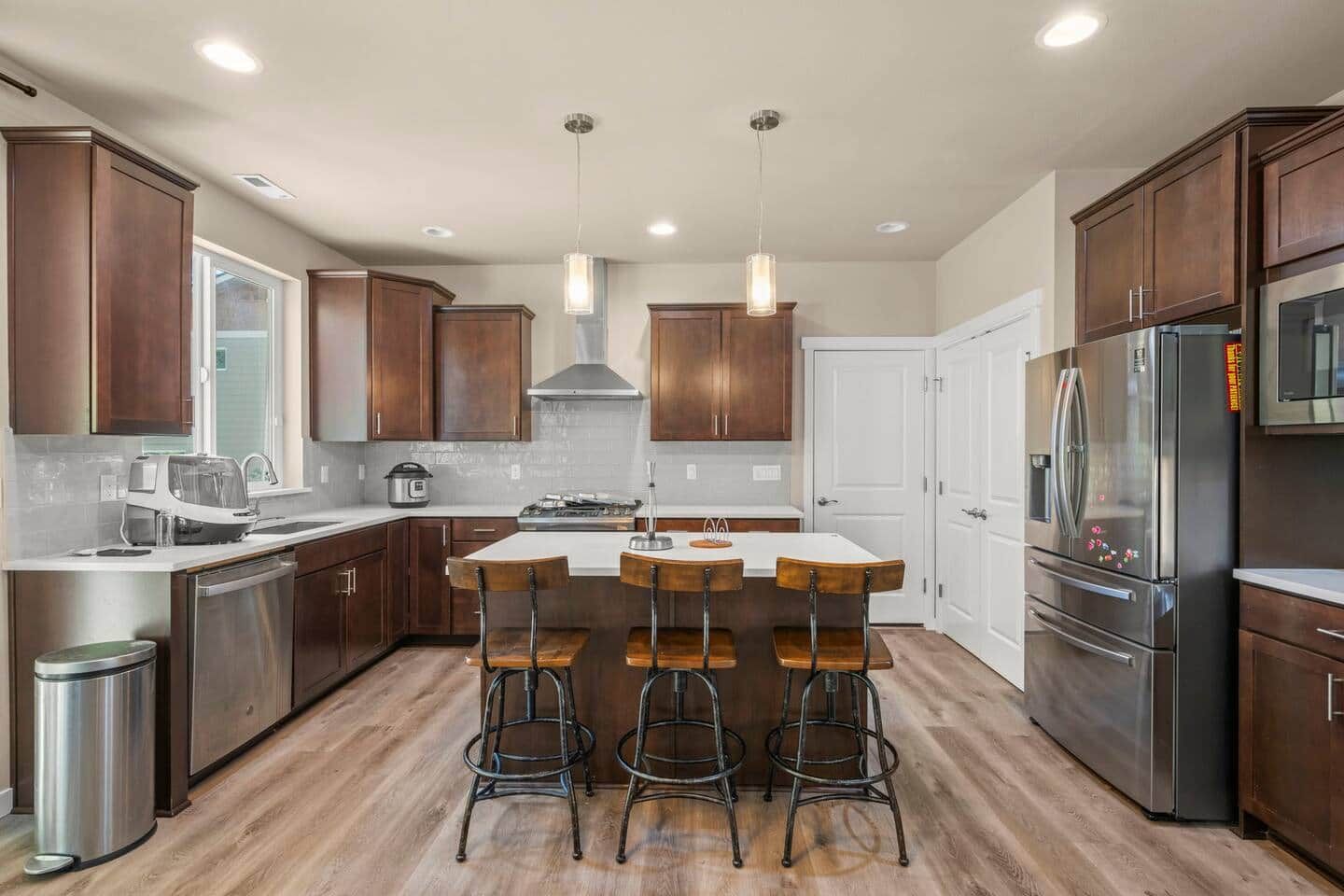 Cocina moderna con armarios de madera oscura, electrodomésticos de acero inoxidable y una isla central con taburetes de bar.