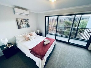 A bedroom with a bed, a nightstand, a lamp, a red throw blanket, and a large window with a view of greenery. - Calm Getaway Close to Airport (Hadfield)