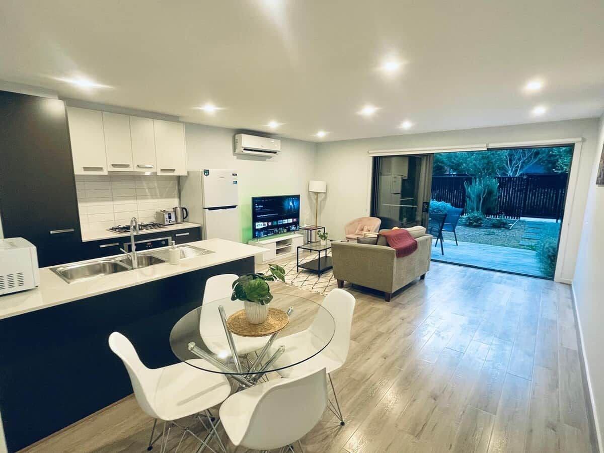 A modern kitchen with a dining area, a TV, and a sliding glass door leading to a backyard.