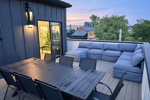 Eine Terrasse mit einem Holztisch, Stühlen, einer eingebauten Sitzecke und einer Glastür zu einem Innenbereich.