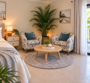 A bedroom with a bed, two patterned armchairs, a round coffee table, a potted plant, and a nightstand with a lamp. - Bay Breeze - Tropical Escape Horseshoe Bay Bowen (Bowen)