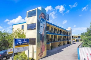 A hotel with a large mural of a person on the side, multiple balconies, and a sign indicating overnight stays are welcome.