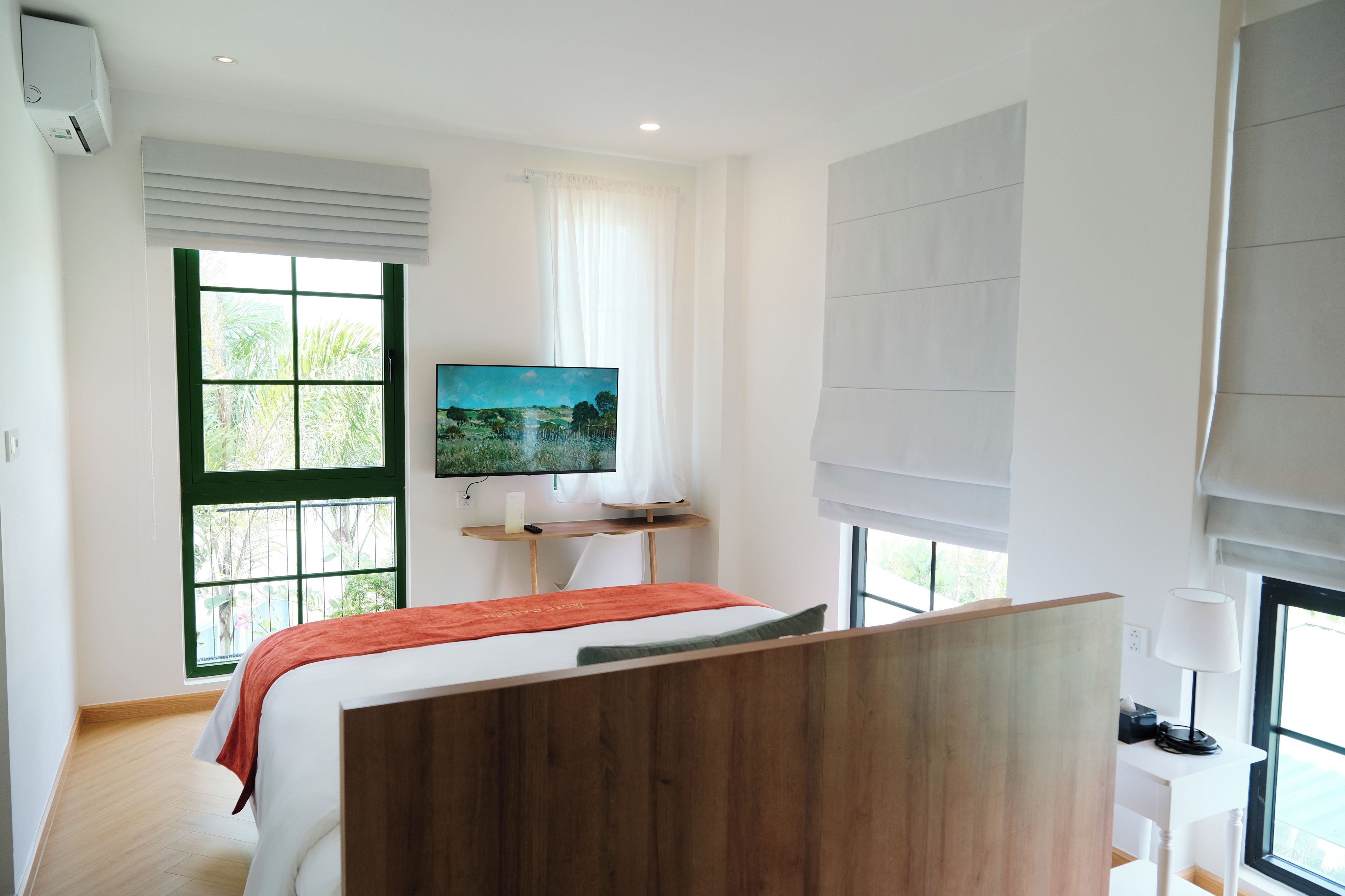 A modern bedroom with a bed, a TV, and a window with a view of greenery.