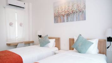 A hotel room with two beds, a window with curtains, an air conditioning unit, a painting on the wall, and a bedside table with a lamp.