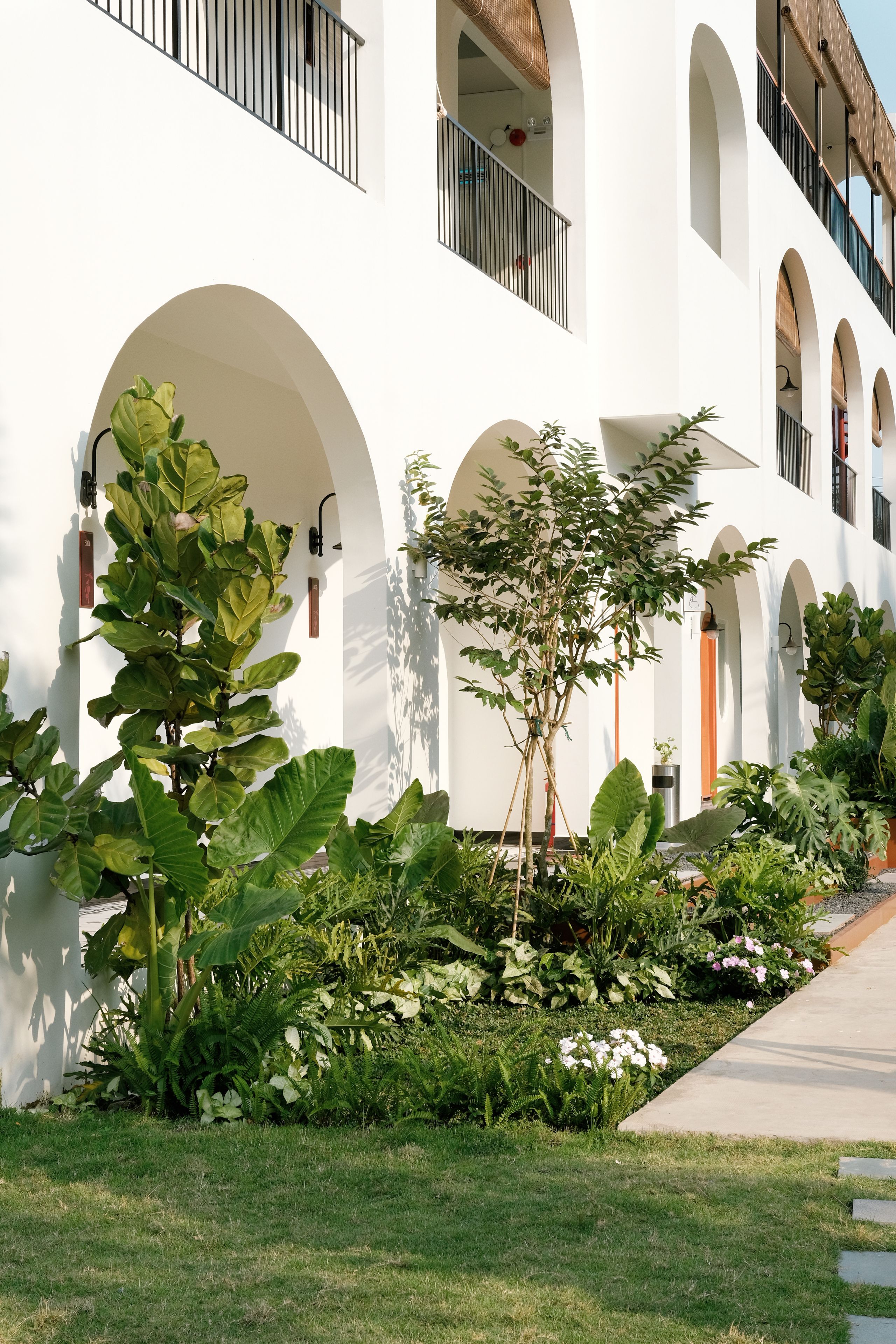 Un edificio con varios ventanales arqueados y un jardín cuidado con diversas plantas y flores.