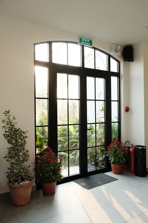 Entrada de hotel con puerta de vidrio, plantas en macetas y extintor.