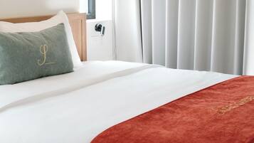 A hotel room with a neatly made bed, a red throw blanket, and a green pillow with a monogram.