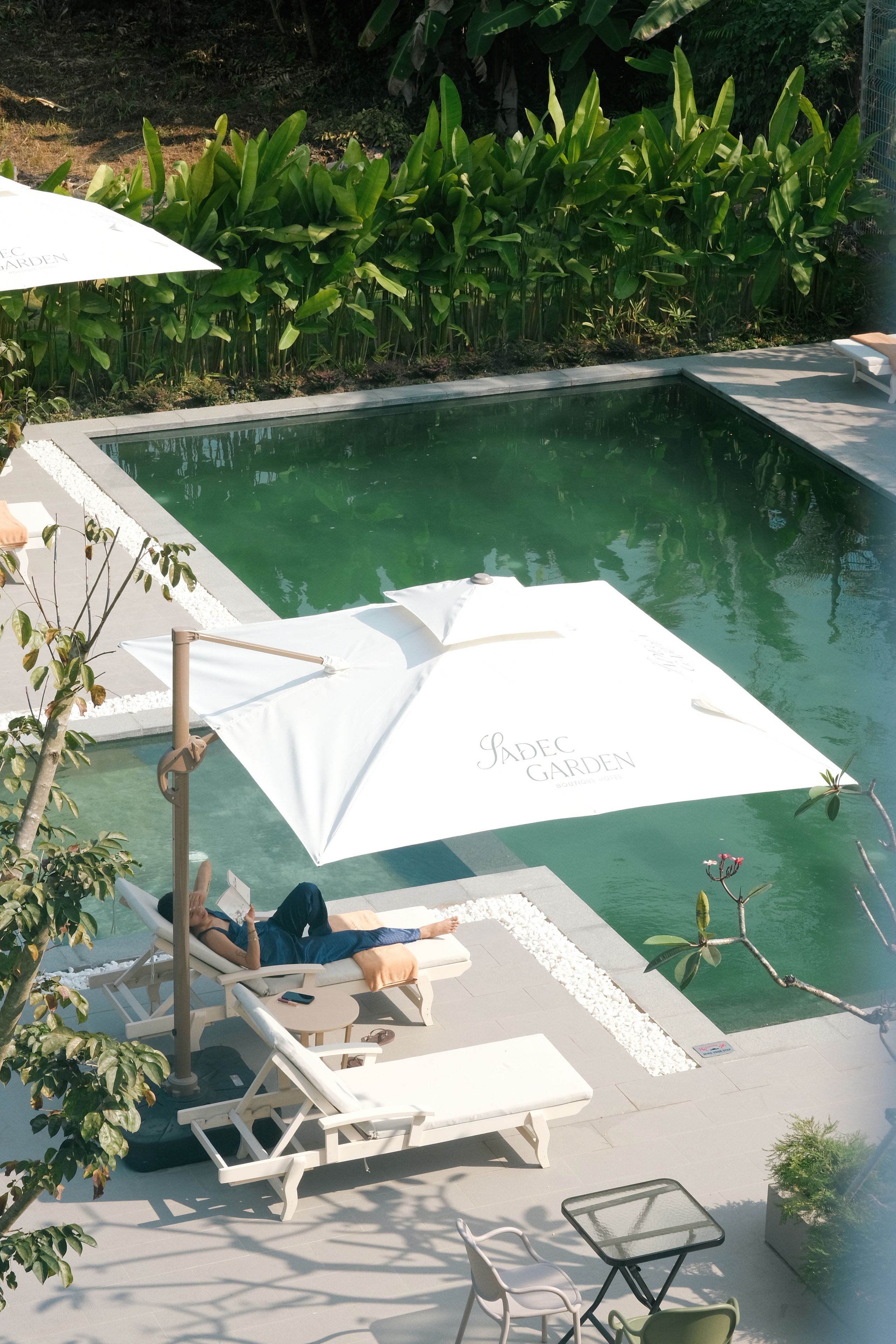 A pool area with lounge chairs and umbrellas, surrounded by lush greenery.