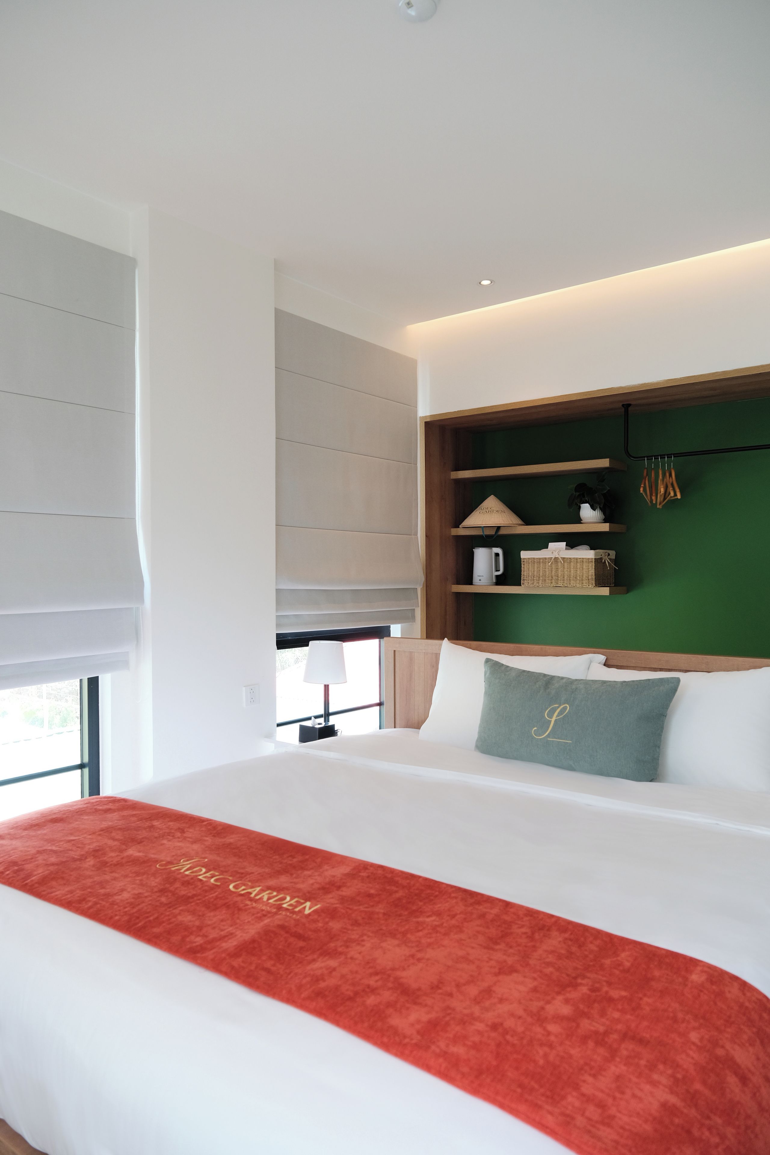 A modern hotel room with a large bed, a green accent wall, and a wooden shelf with decorative items.