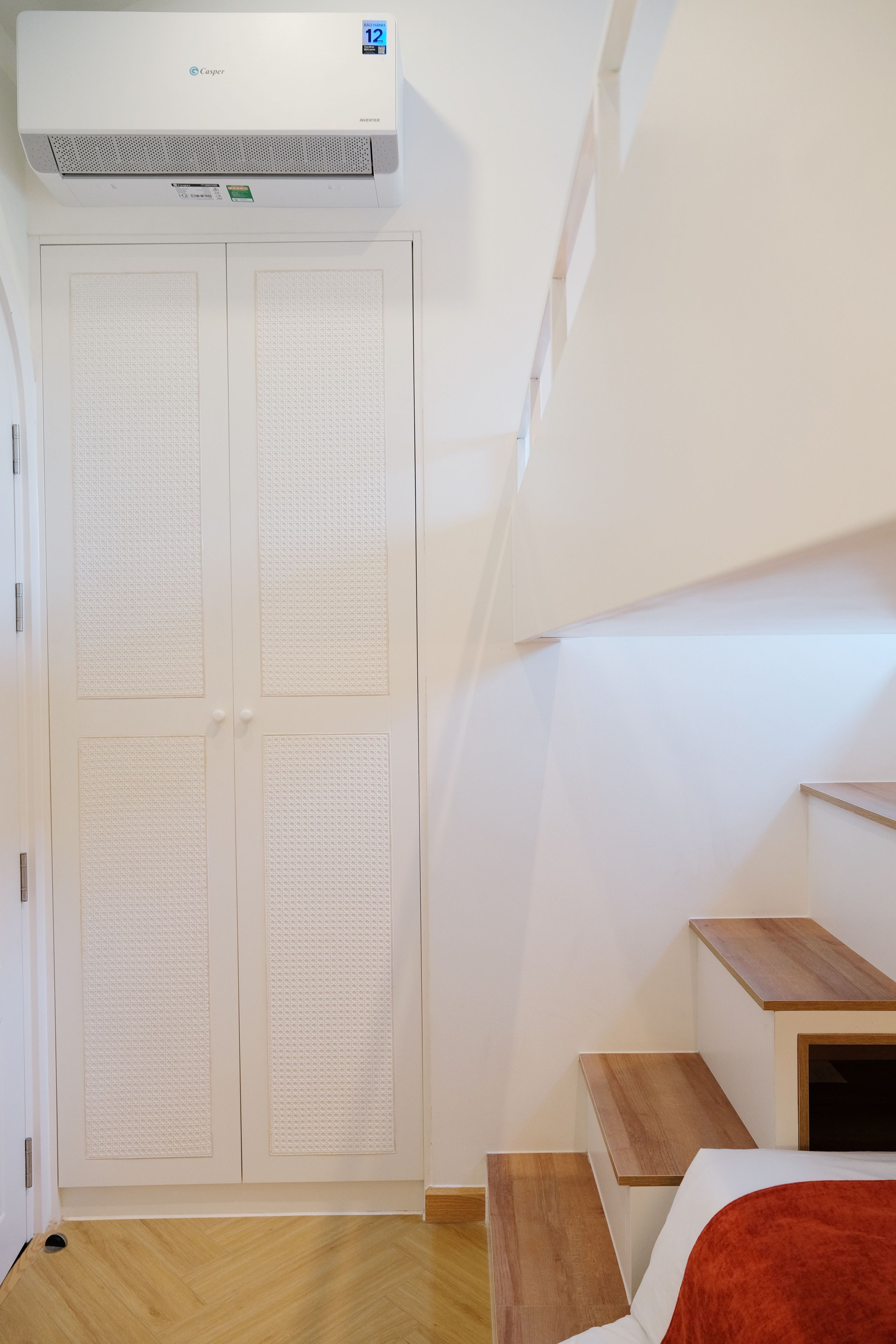 A room with a white wardrobe, a wooden staircase, and a ceiling-mounted air conditioner.