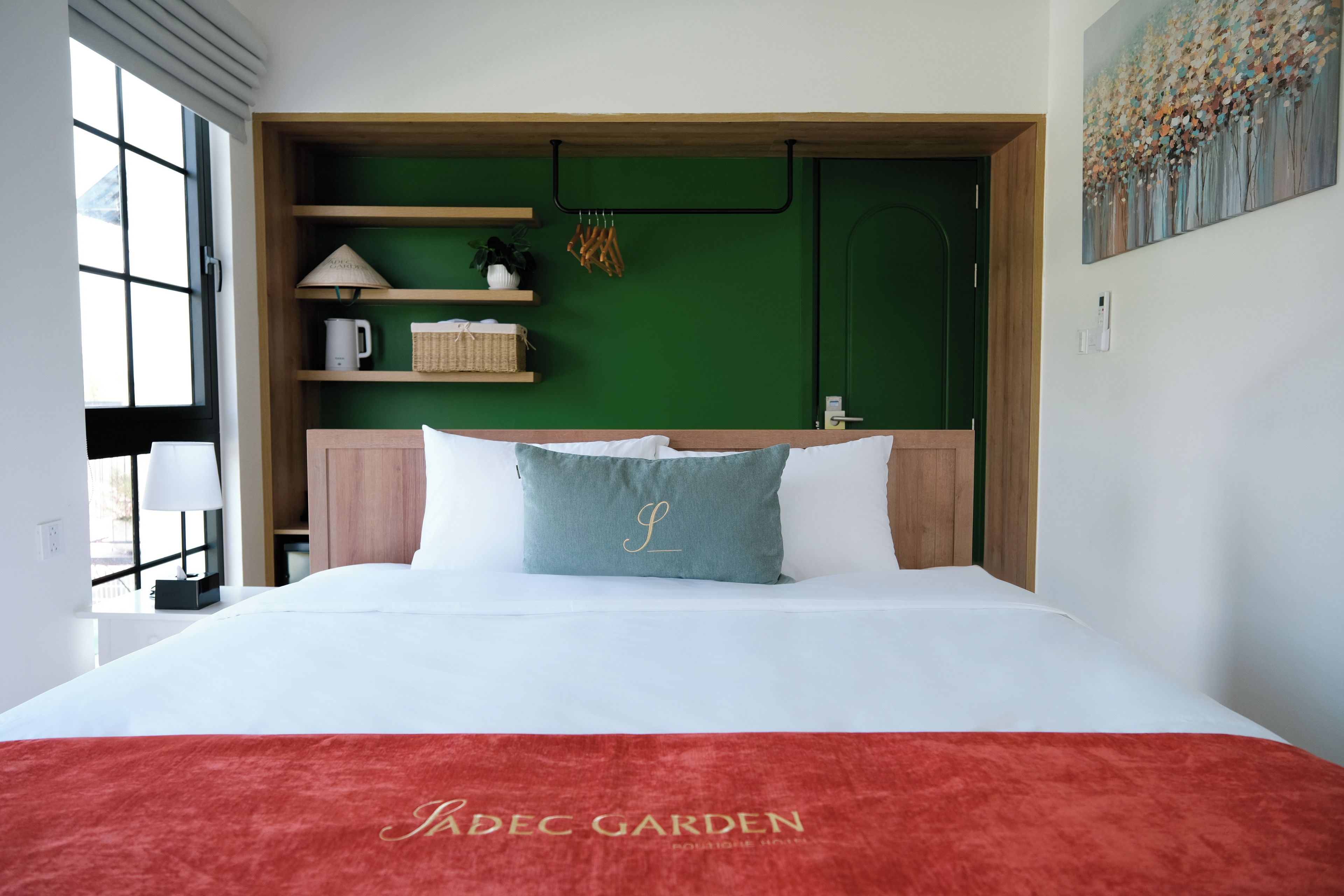 A hotel room with a bed, a green wall, a wooden shelf, and a painting.
