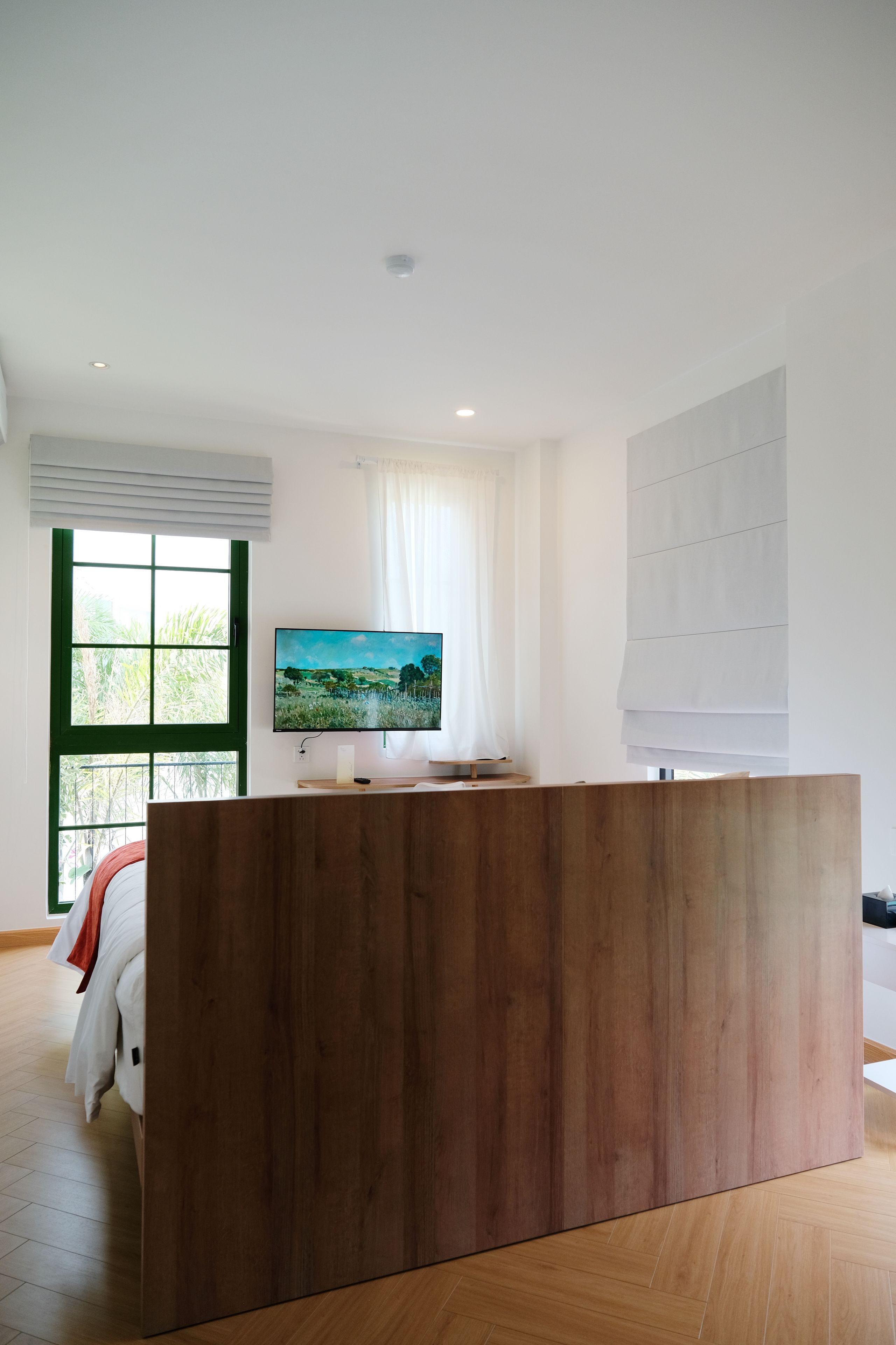 A modern room with a wooden reception desk, a large window with blinds, and a flat-screen TV mounted on the wall.