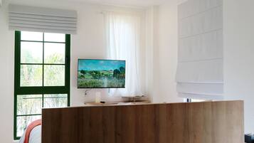 A modern room with a wooden reception desk, a large window with blinds, and a flat-screen TV mounted on the wall.