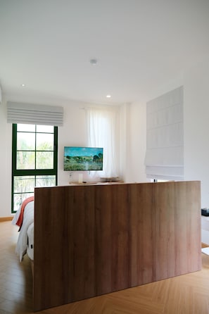 A modern room with a wooden reception desk, a large window with blinds, and a flat-screen TV mounted on the wall.