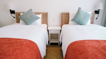 Une chambre d’hôtel avec deux lits, chacun étant agrémenté d’un oreiller orné d’un monogramme.