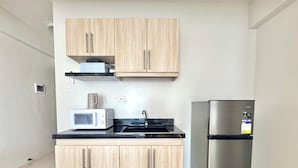Une cuisine compacte avec des meubles de couleur bois clair, un réfrigérateur en acier inoxydable, un four à micro-ondes et un plan de travail noir.