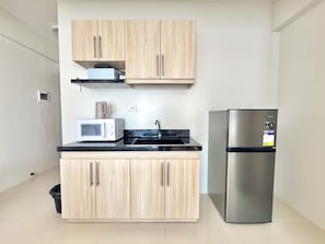 Une cuisine compacte avec des meubles de couleur bois clair, un réfrigérateur en acier inoxydable, un four  à micro-ondes et un plan de travail noir.