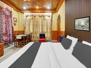 A hotel room with a bed, a dining table with chairs, a red bench, and a wooden door. - Collection O Gorchuk Guwahati (Guwahati)